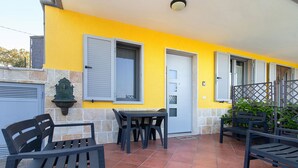 Un bâtiment jaune doté d’un patio carrelé, de sièges en plein air et d’une porte avec une fenêtre.