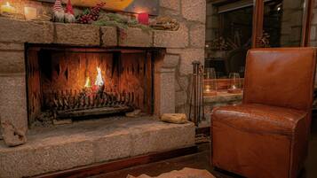 A stone fireplace with a fire, a leather chair, and a rustic decor with candles and gnomes.