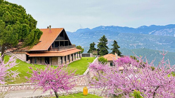 Uma casa com telhado inclinado, paredes de pedra e vista para montanhas.