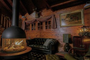 En stuga byggd av timmer med en inredning som inkluderar en öppen spis, en soffa i läder, väggar av trä och en tavla i en ram.