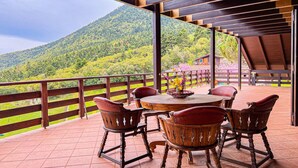 Um terraço com mesa e cadeiras de madeira, vista para uma montanha e um cercado de madeira.