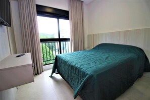 Een slaapkamer met een bed, nachtkastje, raam met gordijnen en balkon.