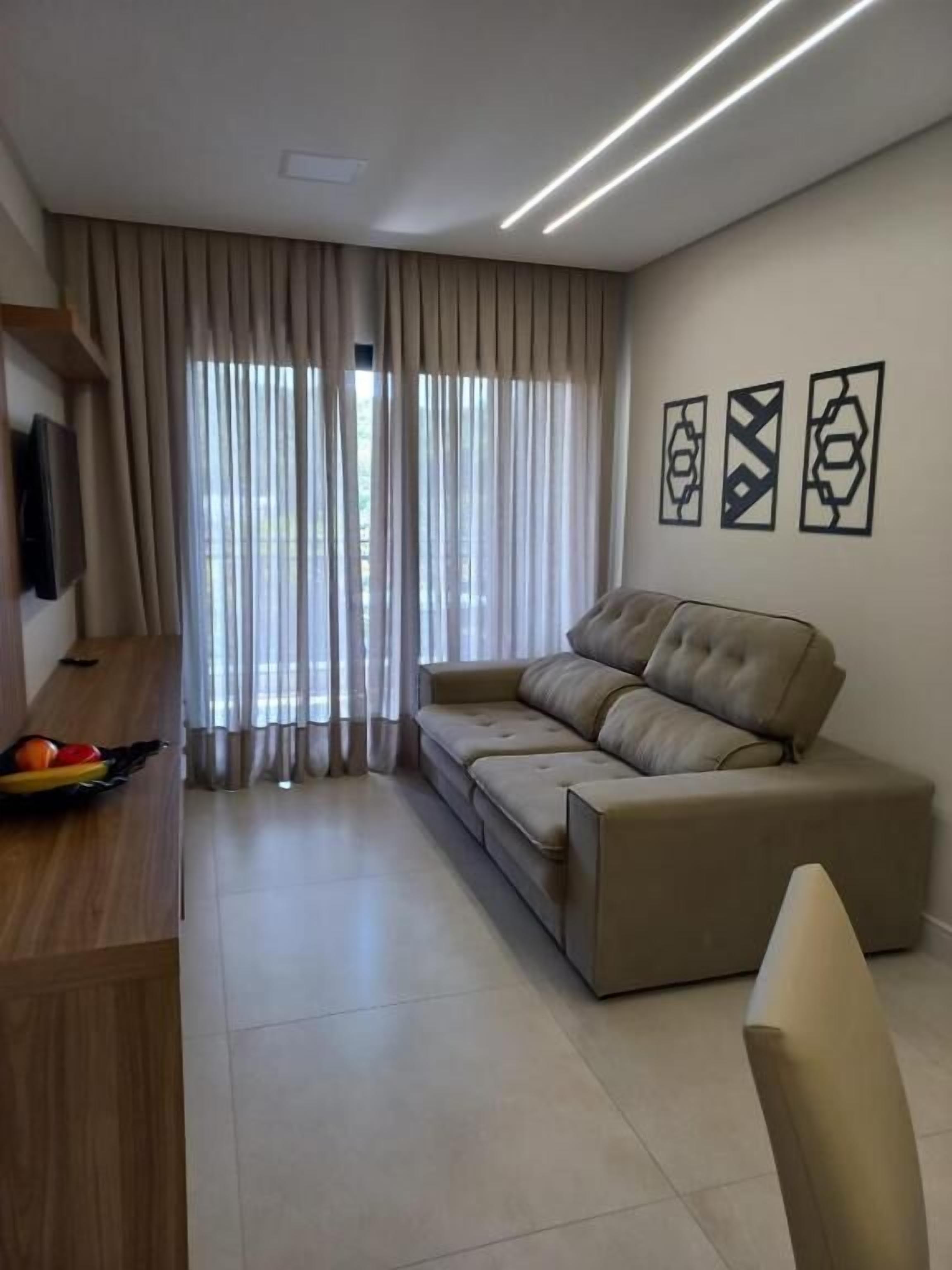 A modern living room with a sofa, a TV mounted on the wall, and a dining area with a table and chairs.
