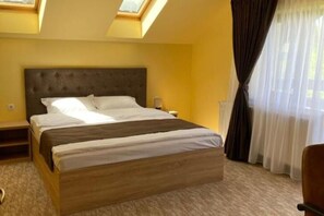 A bedroom with a large bed, a nightstand, a bedside table, and a window with curtains. - BELLESTAY/Suite for 4 (Brașov)