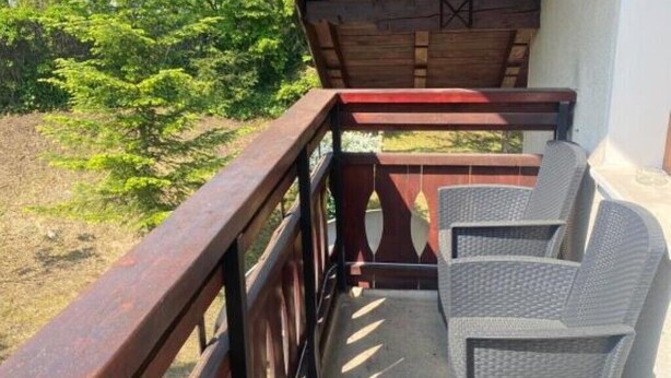 A balcony with a wooden railing, two wicker chairs, and a view of greenery. - BELLESTAY/Suite for 4 (Brașov)