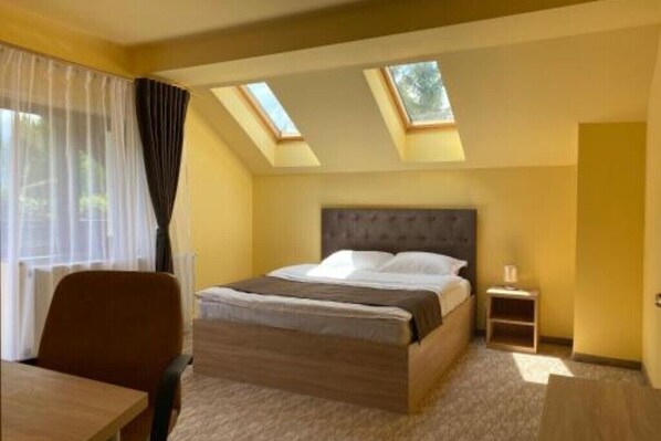 A hotel room with a bed, a desk, a chair, a nightstand, and skylights. - BELLESTAY/Suite for 4 (Brașov)