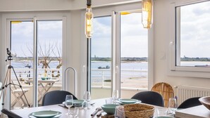 Un coin repas avec une table dressée pour quatre personnes, un télescope et une vue sur une étendue d’eau, visible à travers de grandes fenêtres.
