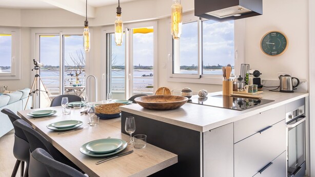 Une cuisine moderne dotée d’un grand îlot central, d’un coin repas et offrant une vue sur l’eau.