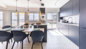 Une cuisine moderne avec des meubles de couleur sombre, un îlot central et un coin repas comprenant des chaises et une table pour quatre personnes.