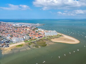 Ein Luftbild einer Küstenstadt mit einem markanten Hotel, einem Sandstrand und einer Marina mit Booten.