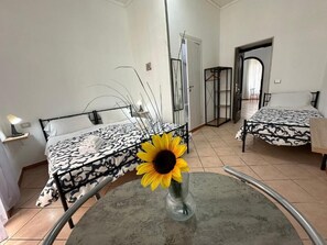 A room with two beds, a round table with a vase of sunflowers, and a door leading to another room. - Stella Sirio Rooms (Naples)