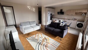 Un appartement moderne comprenant un salon, un canapé, une télévision, une cuisine et un espace buanderie.
