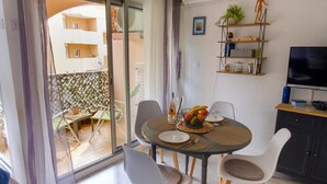 A dining area with a round table, chairs, a television, and a balcony with a view of a building. - Beautiful apartment with sea view and quiet (Sainte-Maxime)