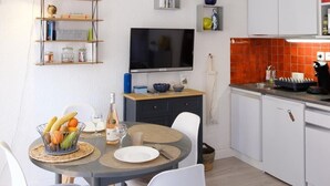 A modern kitchen with white cabinets, a dining area with a round table and chairs, a ceiling fan, and a TV mounted on the wall. - Beautiful apartment with sea view and quiet (Sainte-Maxime)