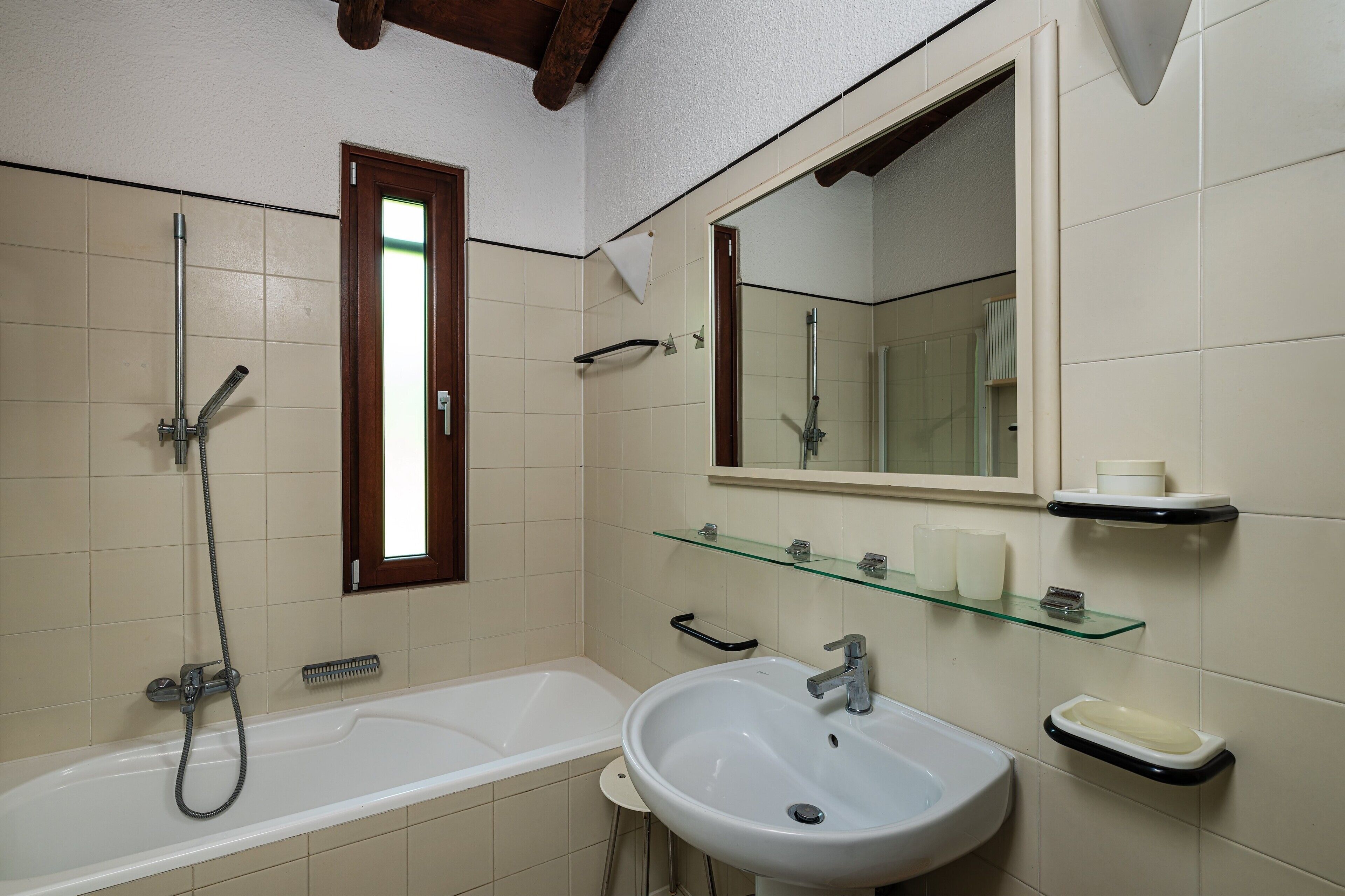 A bathroom with a bathtub, a sink, a mirror, and a glass shelf with toiletries.