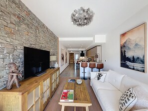 Ein modernes Wohnzimmer mit Steinwand, Fernseher, Holztisch und einer Couch mit Zierkissen.