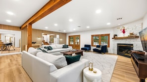 A modern living room with a sectional sofa, a fireplace, and a dining area with a wooden table and chairs.