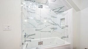 A modern bathroom with a glass-enclosed shower, a white bathtub, and marble-patterned walls. - New! Walk to Water, Shops | Hot Tub, Sauna & Pool (Ellison Bay)