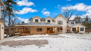 A two-story house with a covered porch and a snow-covered yard. - New! Walk to Water, Shops | Hot Tub, Sauna & Pool (Ellison Bay)
