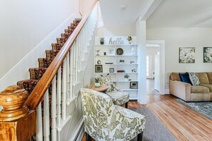 Eine Treppe mit aufwendiger Holzreling, eine weiße Wand mit einem 'hello' Schild, ein Bücherregal und ein beiges Sofa in einem Wohnzimmer.