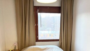 A bedroom with a bed, a bedside table, a window with curtains, and a hanging light fixture. - Bright & Spacious Retreat Near Santa Claus Village (Rovaniemi)