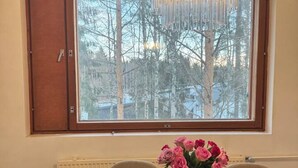 A dining area with a wooden table, chairs, a vase with flowers, a chandelier, and a window with a view of trees. - Bright & Spacious Retreat Near Santa Claus Village (Rovaniemi)