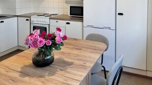A modern kitchen with white cabinets, a stainless steel refrigerator, a microwave, and a wooden dining table with a vase of flowers. - Bright & Spacious Retreat Near Santa Claus Village (Rovaniemi)