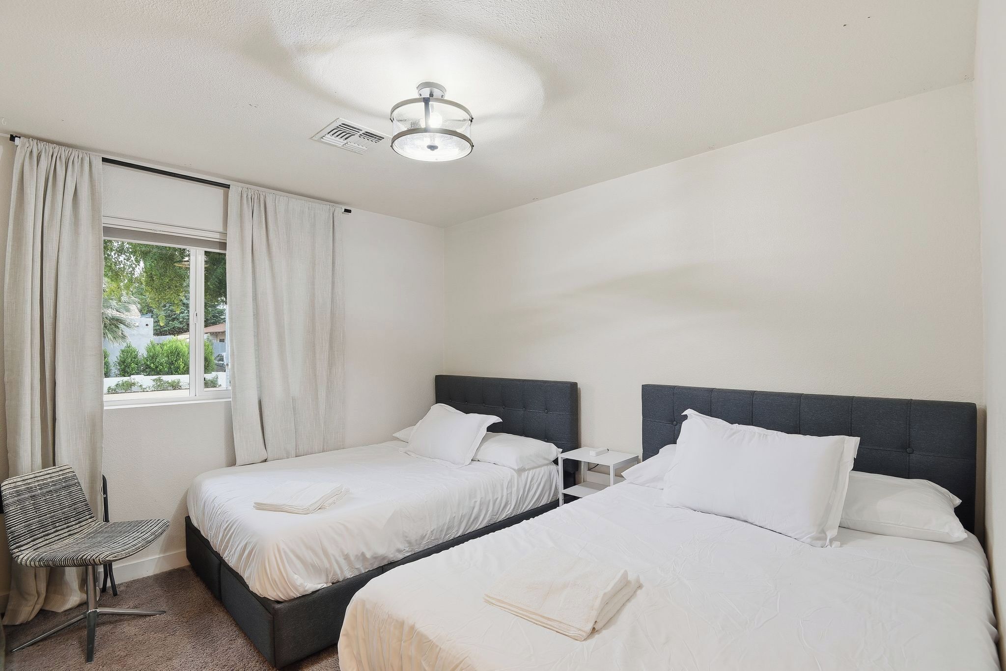 A hotel room with two beds, a chair, a nightstand, and a window with curtains.