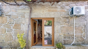 A stone building with a wooden door, a potted plant, and an air conditioning unit. - Casa Da Adega, between the Minho River and the Mountains (Sá)
