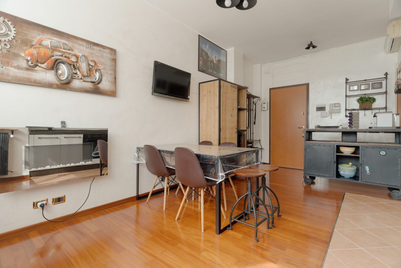 A modern kitchen with a dining area, wooden cabinets, a TV, and a large painting.