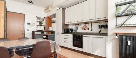 Una cocina moderna con armarios blancos, una mesa de comedor con sillas y un horno empotrado.