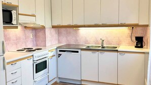 Une cuisine compacte avec des meubles blancs, un four à micro-ondes, une cuisinière, un lave-vaisselle et une machine à café.