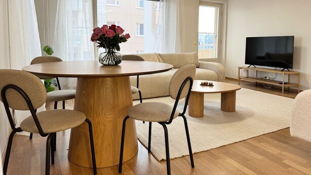 Un salon moderne avec une table ronde en bois, un canapé beige et un téléviseur à écran plat.