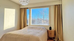 Ein Schlafzimmer mit Bett, Fenster, Nachttisch und einer Pendelleuchte.