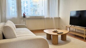 Ein modernes Wohnzimmer mit einer Couch, einem Couchtisch, einem Fernseher und Blick auf ein Gebäude durch große Fenster.