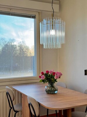 En matplats med ett träbord, stolar, en hängande lampa och ett fönster med utsikt över träd.