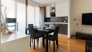 Une cuisine moderne avec des meubles de rangement aux couleurs sombres, une table à manger avec des chaises et un téléviseur à écran plat fixé au mur.