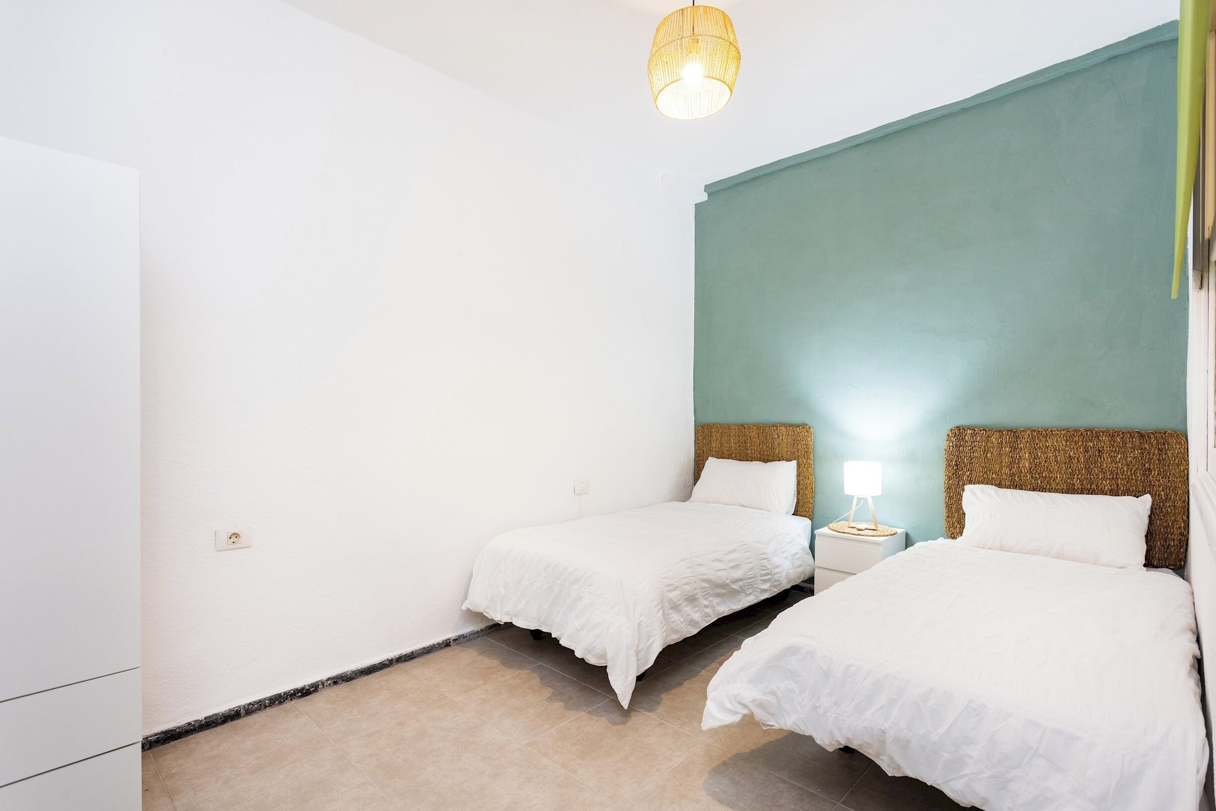 Ein Hotelzimmer mit zwei Betten, einem kleinen Nachttisch mit Lampe und einer Deckenleuchte.