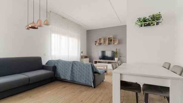 Una sala de estar moderna con un sofá, una mesa de comedor con sillas, un televisor y estantes en la pared con plantas.