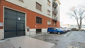 Un edificio con una puerta de garaje grande, una fila de coches aparcados y suelo adoquinado.