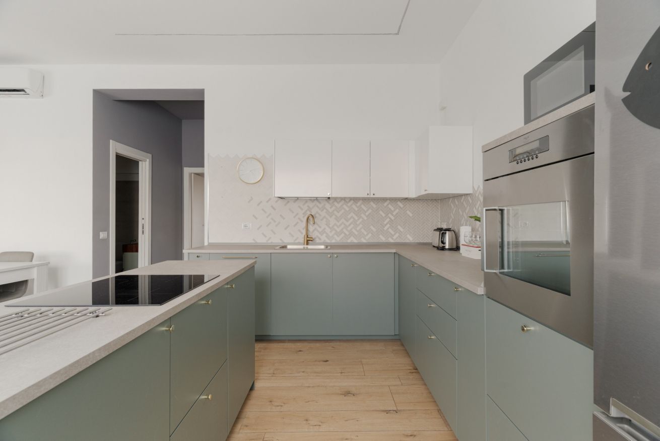 A modern kitchen with grey cabinets, a stainless steel refrigerator, and a herringbone-patterned backsplash.