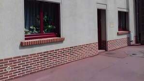 Un edificio con base de ladrillo, una ventana de marco rojo y una puerta.