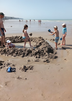 A sandy beach with children playing and building sand structures.