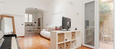 Una sala de estar moderna con un piano, un sofá blanco, un televisor y un ventanal corredero que da a un área exterior.