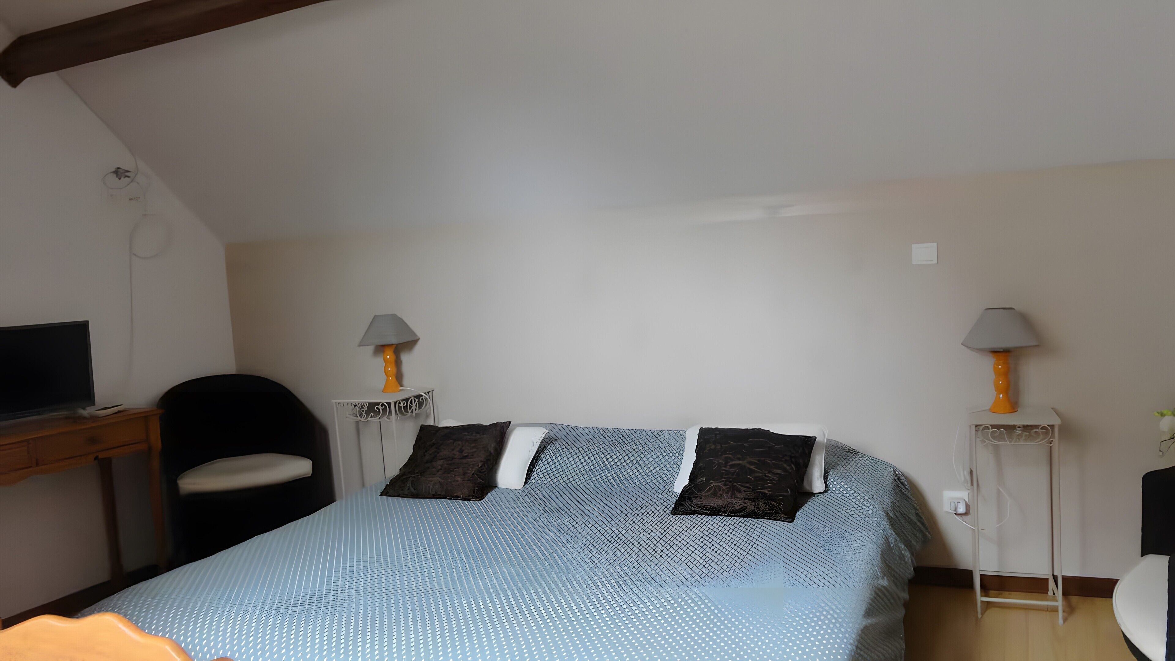 Une chambre à coucher avec un lit, deux lampes de chevet, un bureau avec une télévision et une chaise.