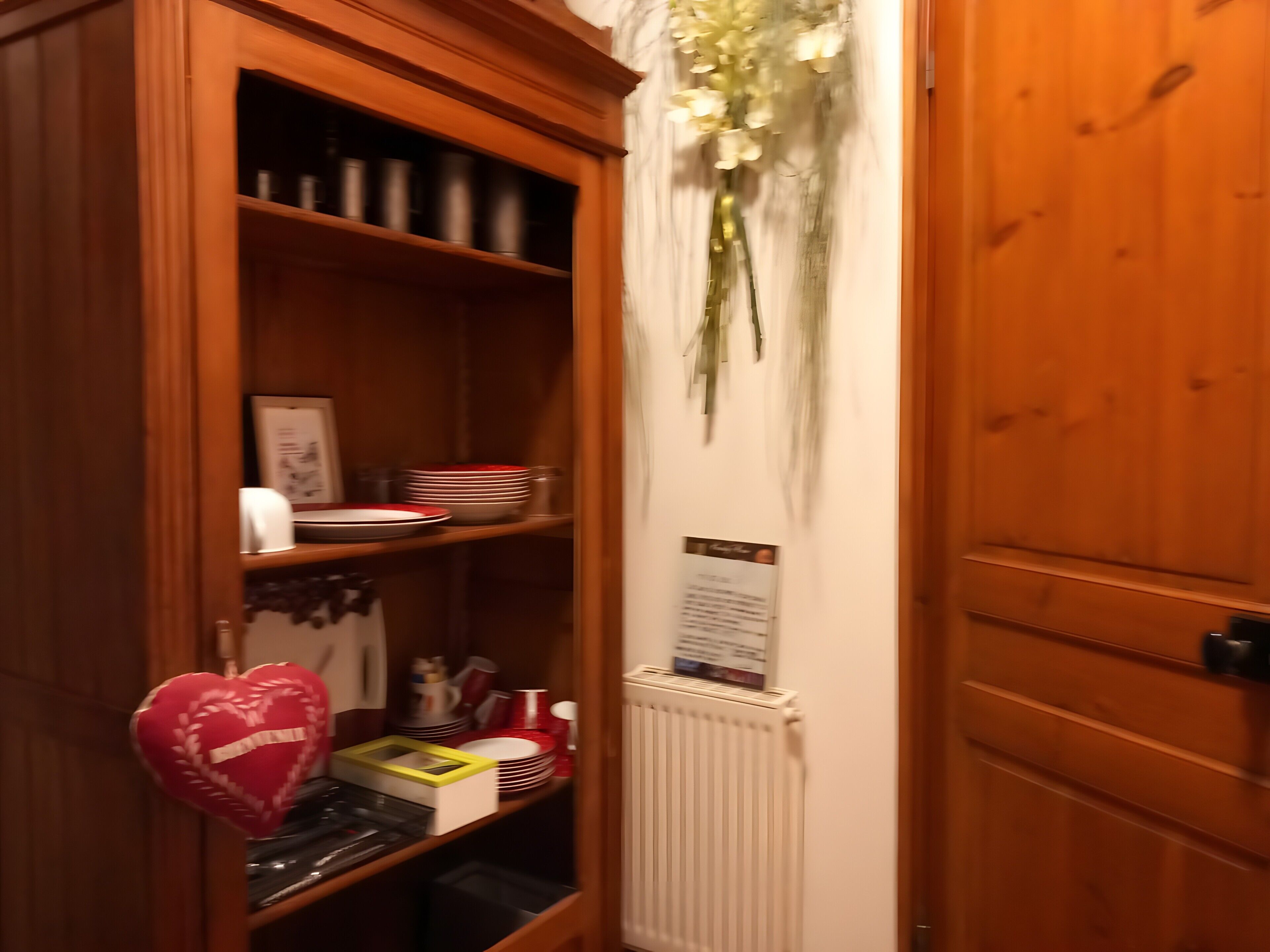 Un gabinete de madera con estantes que contienen utensilios de cocina, un adorno con forma de corazón y un letrero colgado en la pared.