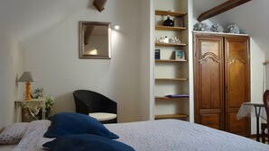 A bedroom with a bed, a chair, a wardrobe, and shelves with various items.