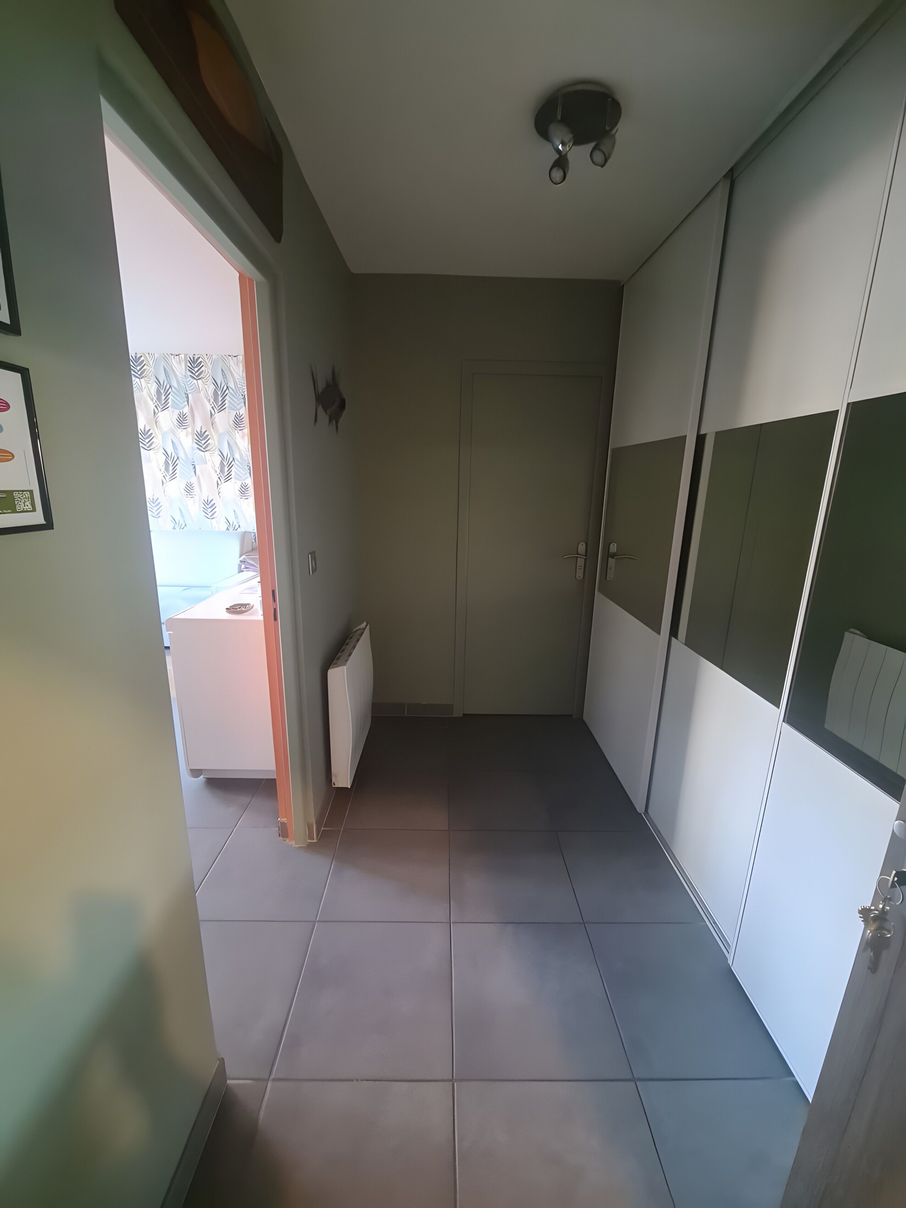A room with a tiled floor, a radiator, a door, and a ceiling fan.