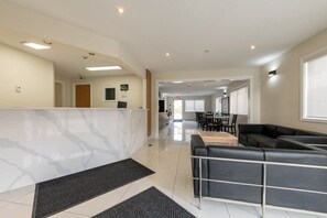 Een moderne hotellobby met een receptiebalie, een zithoek met een bank en een eetgedeelte met tafels en stoelen.