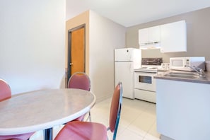 A compact kitchen with a refrigerator, microwave, stove, and sink. There is a dining area with a table and chairs. - Super 8 By Wyndham Golden (Golden)